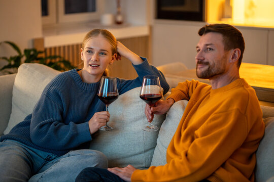 Calm couple unwinding together with glasses of wine during post work downtime at home. Evening relaxation after job on couch, quiet time, alcohol beverages at home, domestic comfort after workday,