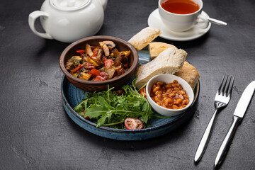 English breakfast with baked beans, ciabatta, and vegetable ragout on black background