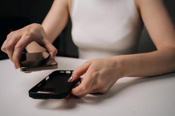 Woman placing new gold smartphone into sleek black phone case with magnetic closure while sitting at white table, showcasing modern technology and stylish accessories.