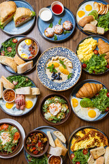 Assorted gourmet breakfast dishes on a rustic wooden table, top view