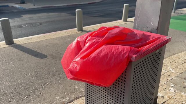 Red plastic trash bag swaying in the wind in a city bin