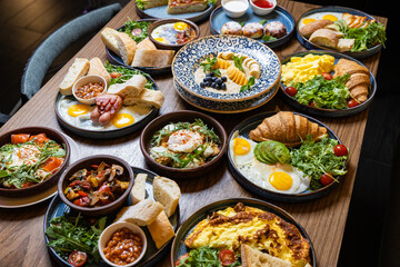 Assorted gourmet breakfast dishes on a rustic wooden table, top view