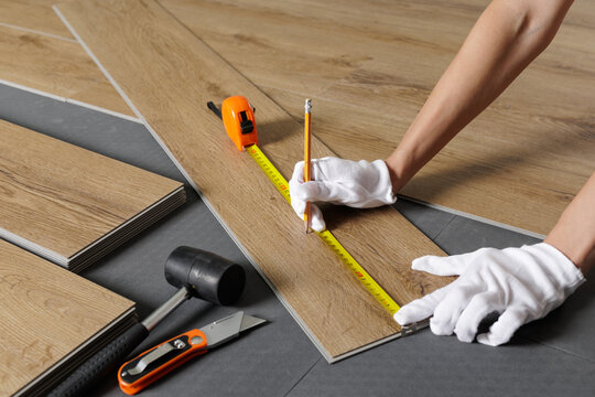 Hands measuring SPC vinyl plank with tape on underlayment during flooring installation - Powered by Adobe