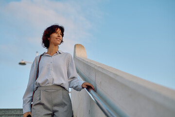 Businesswoman climbing stairs in the city looking up at the sky with positive expression, concept...