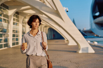 Businesswoman walking with takeaway coffee in the city during sunrise, enjoying a moment of peace...