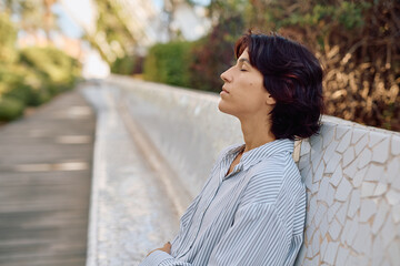 Businesswoman taking a break from work, sitting on a bench with closed eyes, breathing fresh air...