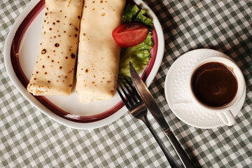 Pancakes - palacinke with fresh tomato and lettuce served next to a cup of strong Balkan coffee. Serbian breakfast in a Balkan cuisine cafe