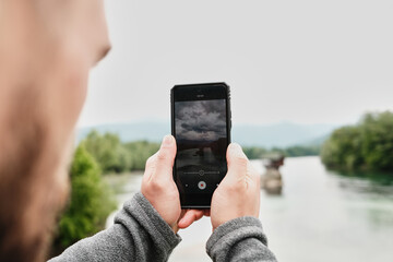 Close-up of a man filming the Drina River house on his phone, capturing the iconic Serbian view. Rear view. A popular tourist destination. Serbia country in spring season