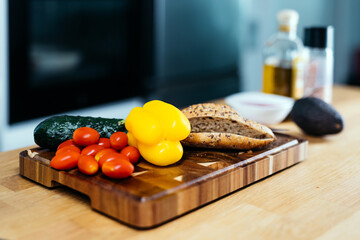 Fresh vegetables including yellow bell pepper, cherry tomatoes, cucumber, and whole grain bread...