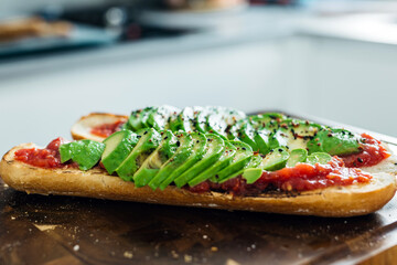Freshly sliced avocado on toasted bread with tomato spread, garnished with black pepper, showcasing a vibrant and healthy culinary creation in a modern kitchen setting
