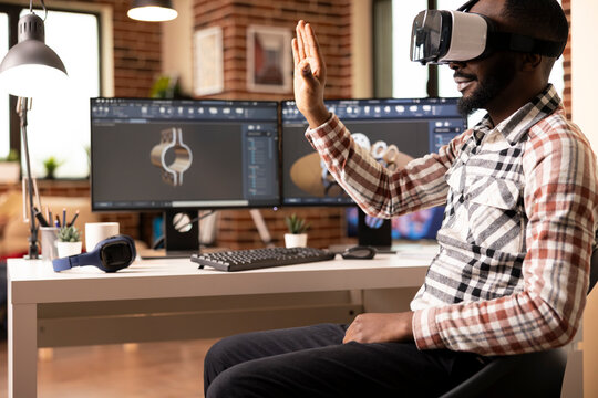 African american man wearing VR headset while seated at desk, remotely creating 3d clamps prototypes for construction company. Innovative design process using virtual reality tools.