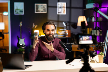 Influencer in neon lit home studio filming smart light bulb review for online streaming platforms with professional camera. Online star films IoT home automation product with specialized equipment