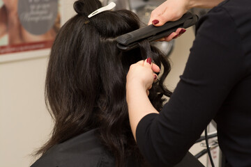 Fototapeta premium Hair stylist making ringlets to brunette woman. Hairdresser working with beautiful woman hair in hairdressing salon.