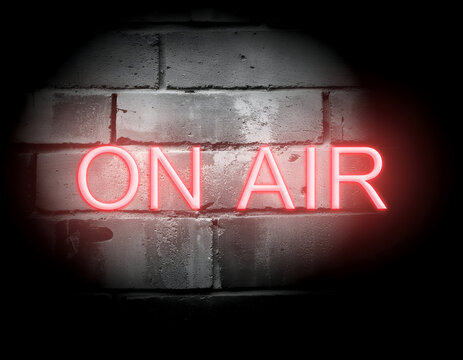 Red neon 'ON AIR' sign glows intensely on a dark, textured brick wall, symbolizing live broadcast, media, and recording studio sessions.