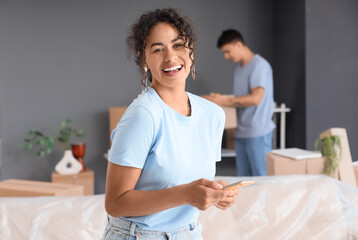 Young African-American woman using mobile phone in room on moving day