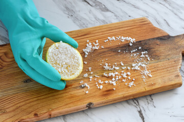 Closeup of person’s hand in protective rubber glove scrubbing wooden cutting board with half...