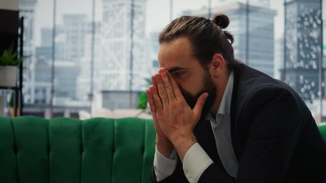 Male corporate leader buries his face in his hands due to frustration, pressure of a declining economy and battling the stress of a failing company. Business downfall and bankruptcy. Camera A.
