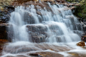Fototapeta premium Smooth Waterfall Cascading Over Mossy Rocks in Forest Setting