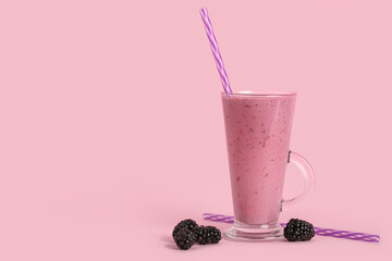 Glass cup of fresh blackberry smoothie and berries on pink background