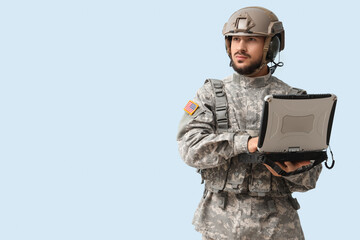 Male soldier working with military laptop on light background