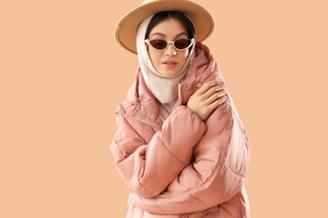 Fashionable young woman in stylish puffer jacket on beige background