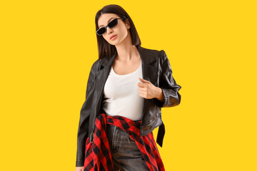 Young woman in stylish leather jacket on yellow background