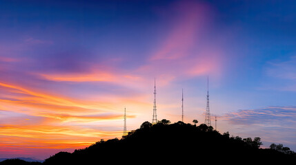 Stunning silhouette of communication towers on hilltop against vibrant sunset sky, showcasing blend of colors that evoke sense of tranquility and connection