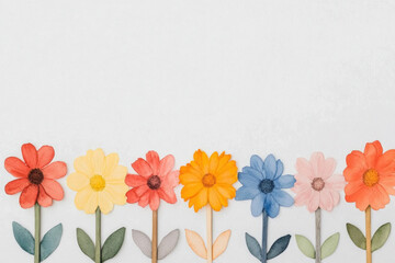 Obraz premium Colorful paper flowers stand in a row against a white backdrop, bright petals in red, yellow, blue, pink, and orange, creating a playful springtime composition with soft shadows.