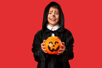 Cute little happy boy dressed as magician for Halloween with basket of candy corns on red background