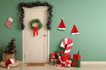 Interior of festive hallway with Christmas tree, gift boxes, candy cane pinata and wreath hanging...