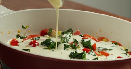 Side view Tomatoes saut ed with green spinach leaves in a nonstick pan, the chef pours in cream and water and stirs the tomatoes with a wooden spatula.Concept for home cooking and culinary inspiration