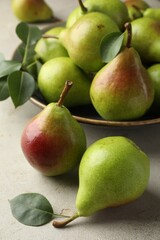 Fresh ripe pears and green leaves on light grey table, closeup