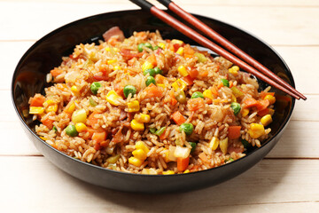 Tasty fried rice and chopsticks on light wooden table, closeup