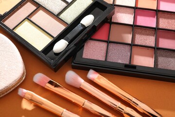 Eyeshadow palettes and brushes on orange background, closeup. Makeup cosmetics