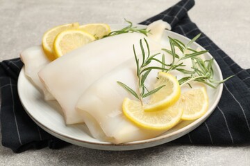 Pieces of raw squids with rosemary and lemon on grey textured table, closeup