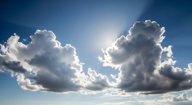 Large cumulus clouds backlit by the sun against a vibrant blue sky, showcasing dramatic light and shadow patterns.