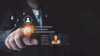 Fototapeta premium A man in a suit points at a futuristic interface with human resource management icons and checkmarks on a dark background.
