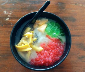 Es Teler, a popular Indonesian dessert served in a black bowl, featuring shaved ice with toppings such as jackfruit, grass jelly, tapioca pearls, and sweet condensed milk.