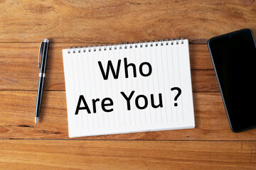 Selective focus of a pen, smartphone and notebook written with Who Are You? on wooden background.