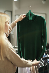 A girl tries on a striped sweater in a store. A young woman chooses clothes in a store while shopping. Seasonal holiday discounts on purchases. Black Friday