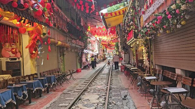 Morning view of the deserted Hanoi Train Street, Vietnam with railway tracks flanked by cafes and colorful lanterns.