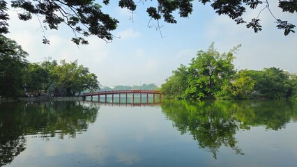 Hoan Kiem Lake in Hanoi, Vietnam, with the iconic red The Huc Bridge reflecting on the calm water.