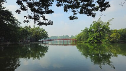 Hoan Kiem Lake in Hanoi, Vietnam, with the iconic red The Huc Bridge reflecting on the calm water.