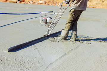 Worker smooth wet concrete at job site on works day, getting surface ready for finishing.