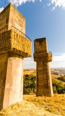 Two beige stone towers, topped with hay bales, stand on a hillside, overlooking a golden, rolling landscape