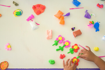 Top view of children making colorful playdough flowers in classroom, creative handmade clay art, preschool education and craft skills, learning activity with modeling clay.