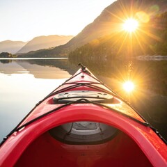 Red kayak floats on calm water with mountains in background and sunlight shining brightly over the serene landscape