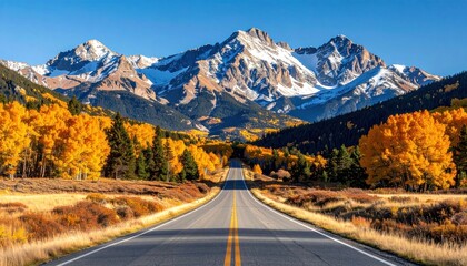 Naklejka premium Winding asphalt road leads to majestic snowy mountains framed by vibrant golden autumn foliage under a clear blue sky, offering scenic drive