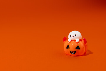 Fototapeta premium playful ghost figurine sitting inside a smiling jack-o’-lantern pumpkin, lit against a bright orange background. The Halloween-themed decoration casts a dramatic shadow