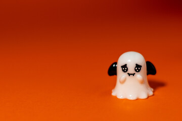 Adorable ghost figurine with black bat wings on an orange background under dramatic spotlight. Playful Halloween-themed decoration, perfect for seasonal advertising, greeting cards, party invitations